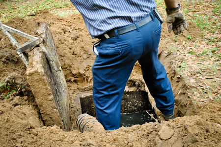 Worker standing at an open excavated septic tank