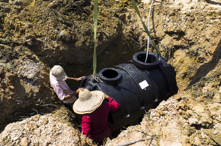 Crew lowering a new black septic tank into an excavated site